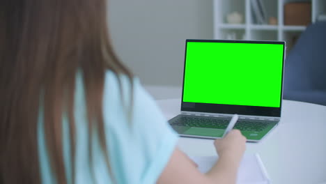 Mädchen-Macht-Sich-Notizen-Im-Notizblock-Vom-Grünen-Mockup-Bildschirm-Des-Laptop-Computers.-Mädchen-Lernt-Online-Am-Computer